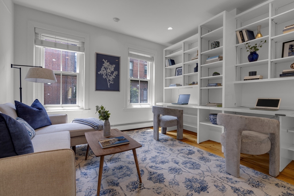 Staged home office with built-in white shelving, two desks, and a seating area.
