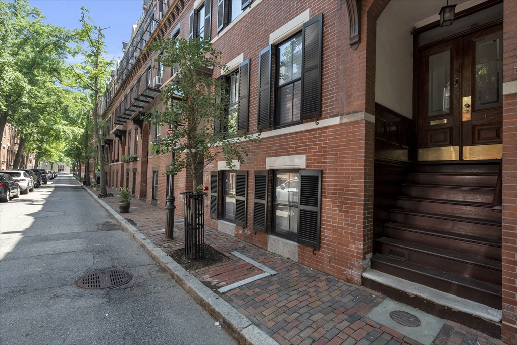 Red-brick rowhouse with black shutters and a recessed wood entrance on a tree-lined street.