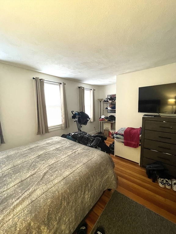 Bedroom with a large bed, two curtained windows, hardwood floors, and a television on a dresser.