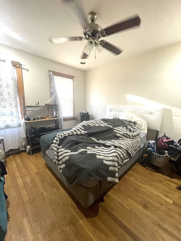 Bedroom with a patterned blanket on the bed, hardwood floors, and a ceiling fan.