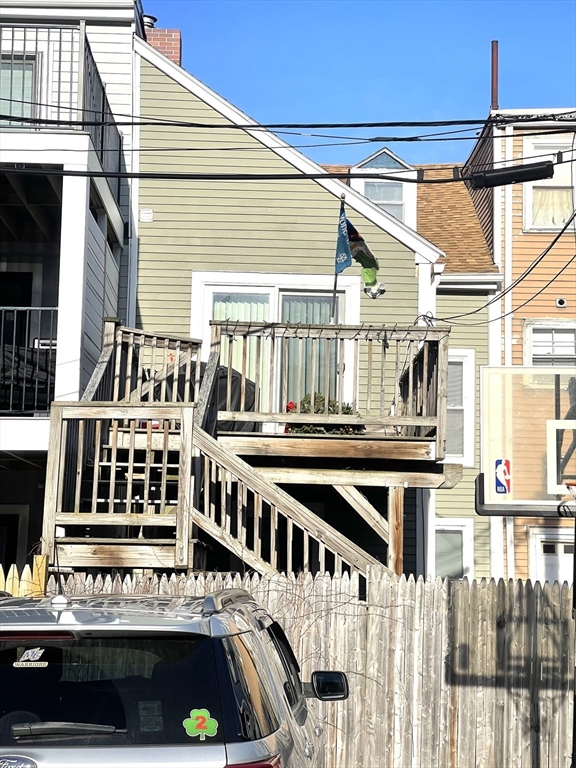 House rear with a raised wooden deck and stairs behind a weathered privacy fence.