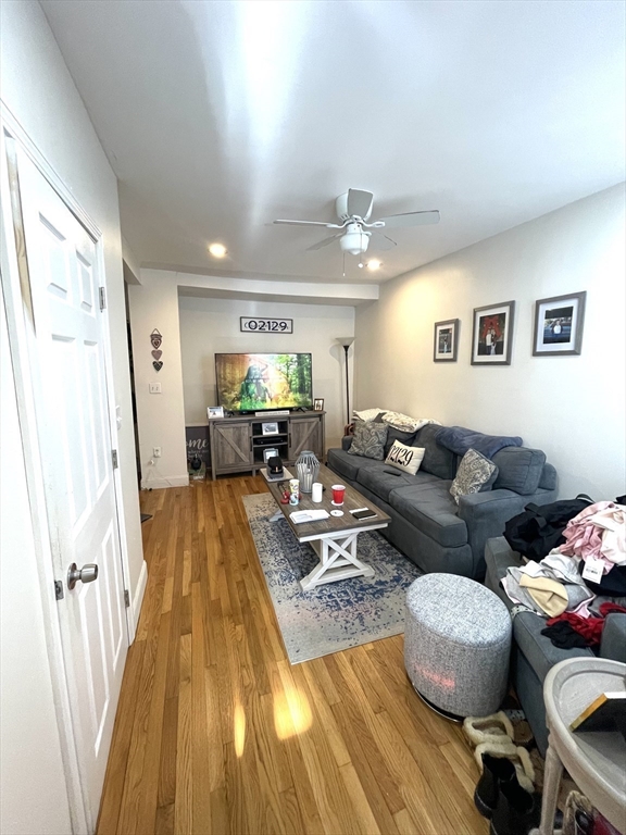 Living room with a gray sectional, hardwood floors, patterned rug, and ceiling fan.