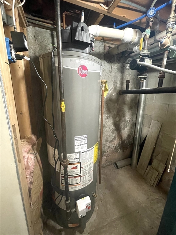 Basement water heater with exposed plumbing and unfinished stone walls.