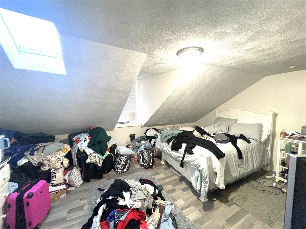Attic bedroom with a skylight, sloped ceiling, and belongings piled around the bed.