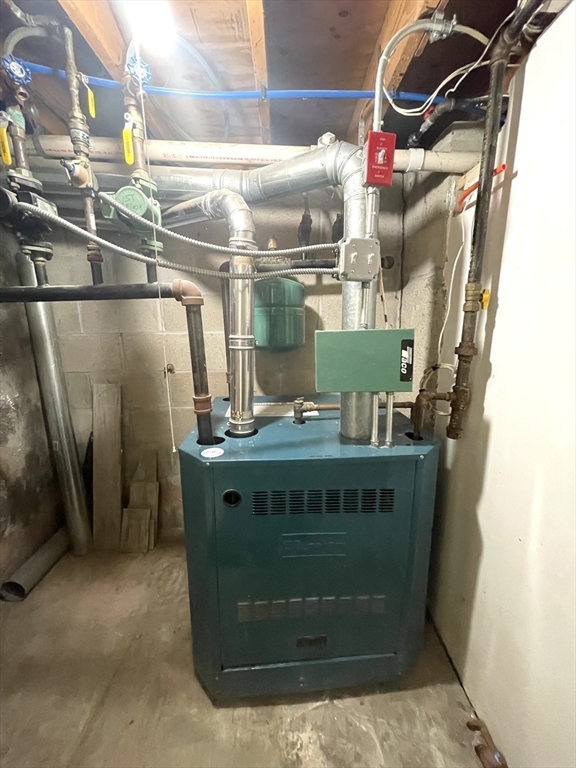 Basement boiler surrounded by exposed pipes and utility equipment.