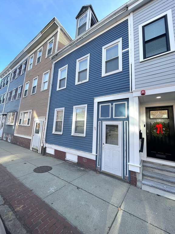 Blue three-story townhouse with white trim and entry door beside attached homes on a city sidewalk.