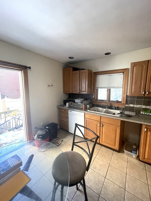 Kitchen with wood cabinets and tiled floor, featuring a sink beneath a window and a sliding glass door.