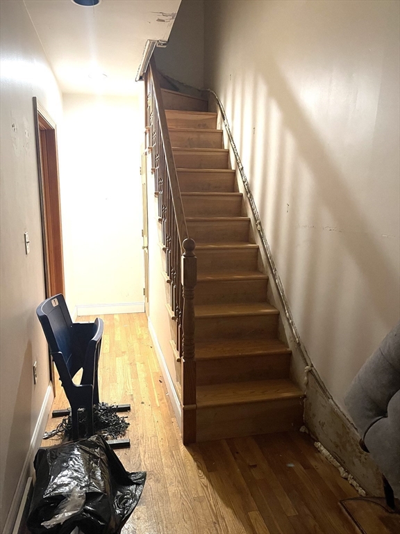 Hallway with a wooden staircase, hardwood floor, and damaged wall along the stairs.