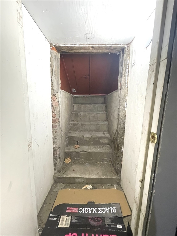 Unfinished basement stairwell with worn concrete steps and a dark red door at the top.