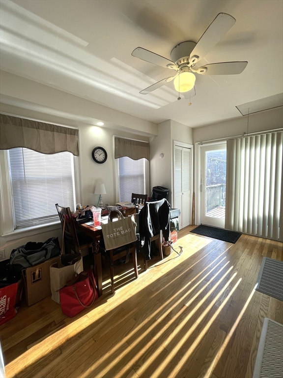 Dining area with a table, ceiling fan, and sunlit hardwood floors beside a balcony door.