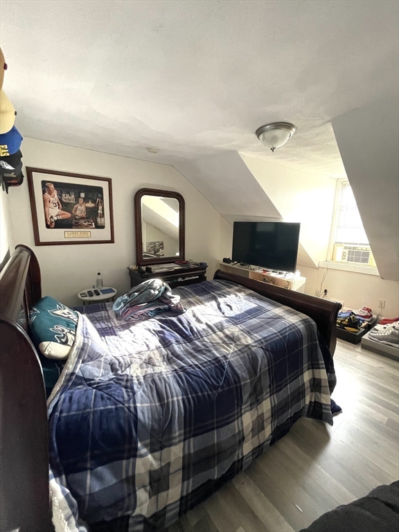 Bedroom with blue plaid bedding, a dresser and mirror, and a television beneath a sloped ceiling.