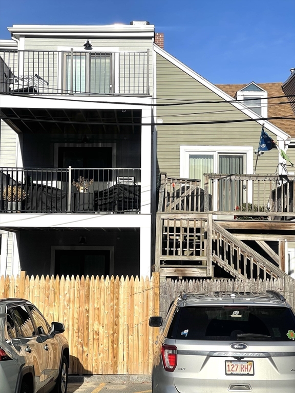 Rear of a multi-story home with stacked balconies, wooden deck stairs, and a picket fence.