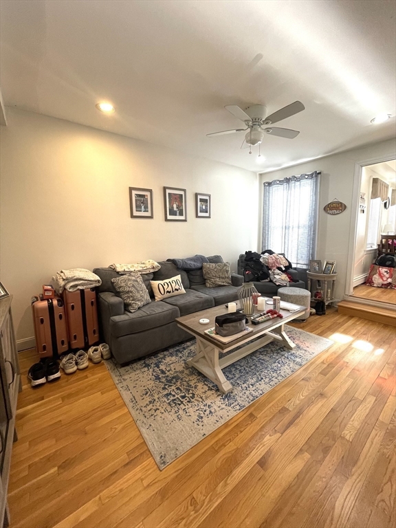 Living room with a gray sectional, patterned rug, hardwood floors, and ceiling fan.