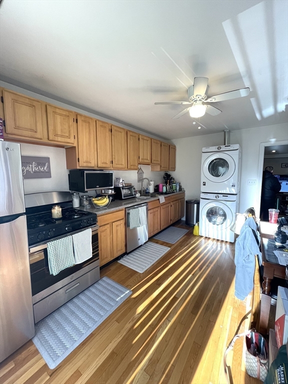 Kitchen with wood cabinets, stainless appliances, stacked washer and dryer, and hardwood flooring.