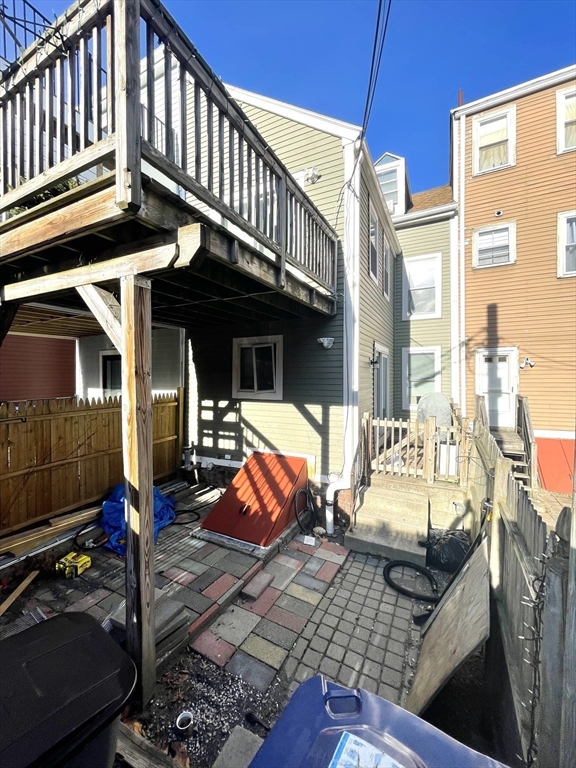 Rear courtyard with a raised wooden deck, paved patio, and neighboring attached homes.