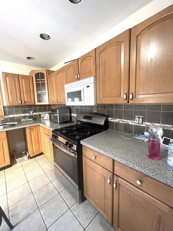 Kitchen with wood cabinets, speckled counters, and a gas range beneath a built-in microwave.