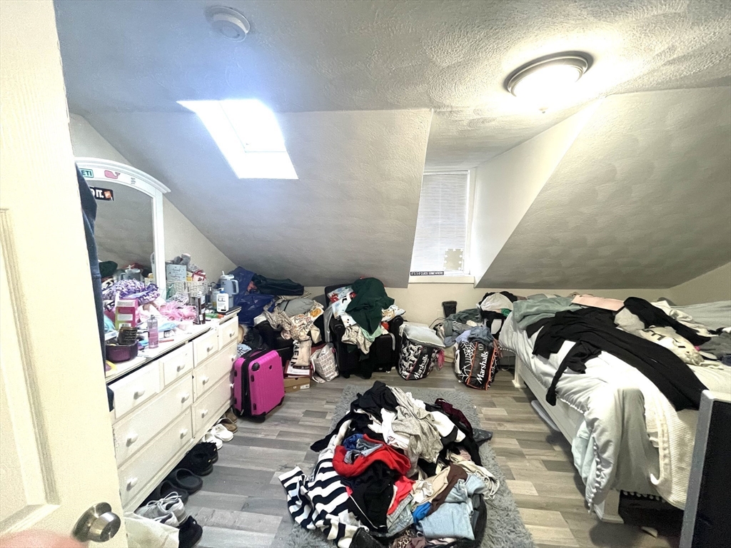 Attic bedroom with a skylight, sloped ceiling, and belongings piled around the bed.
