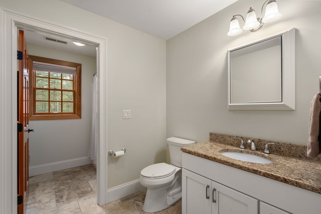 Bathroom with granite vanity, framed mirror, toilet, and a wood-trimmed window in the adjoining bathing area.