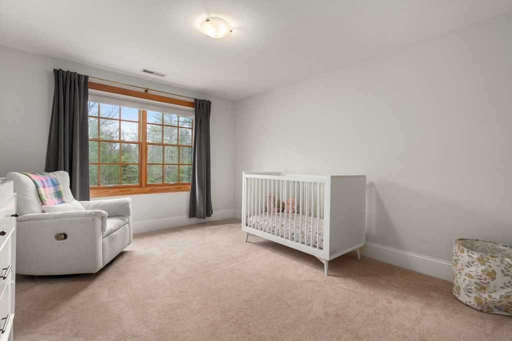 Nursery with a white crib, gray glider, and large wood-trimmed window overlooking trees.