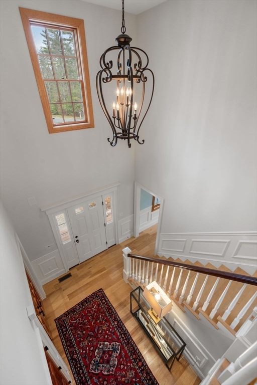 Two-story foyer with a white staircase, hardwood floors, a red patterned runner, and a hanging chandelier.