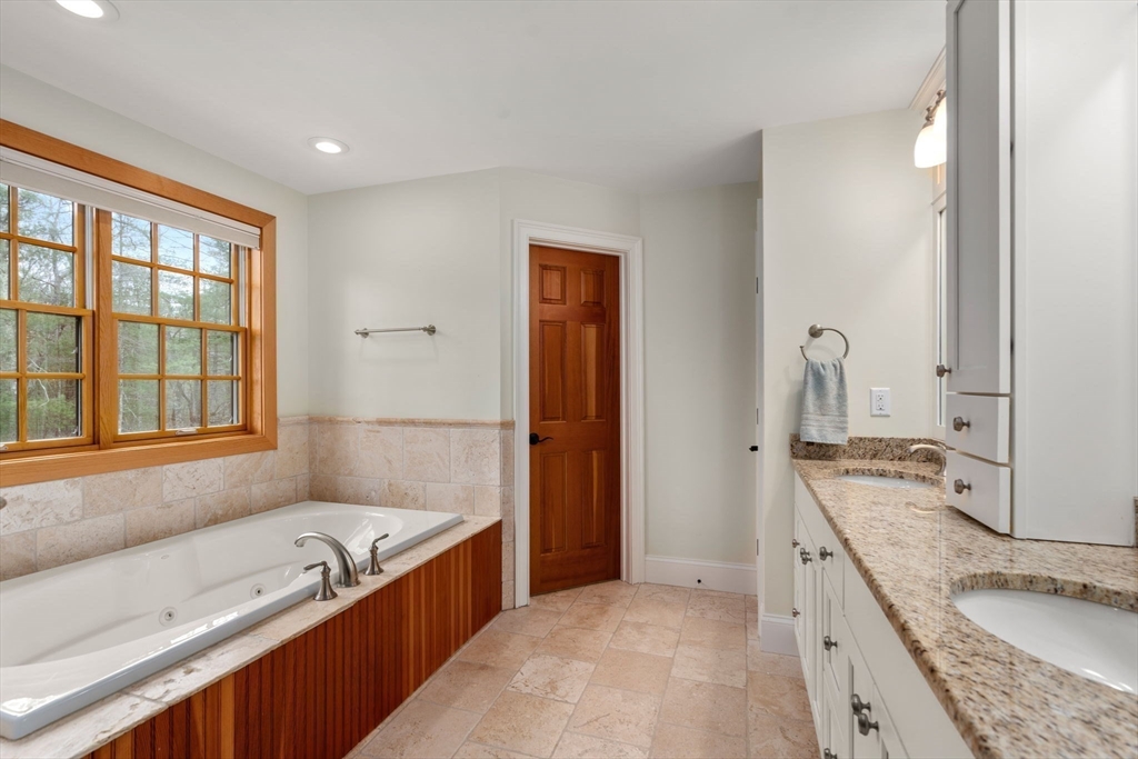 Bathroom with a built-in soaking tub beneath a large wood-trimmed window and a granite vanity.