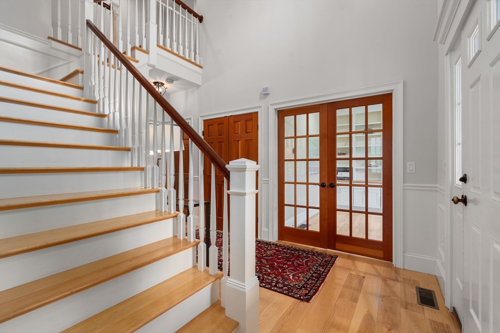 Foyer with a wood staircase, hardwood floors, and glass-paneled French doors opening to the kitchen.