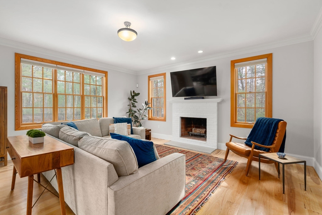 Living room with white brick fireplace, large wood-trimmed windows, pale sectional, and patterned rug.