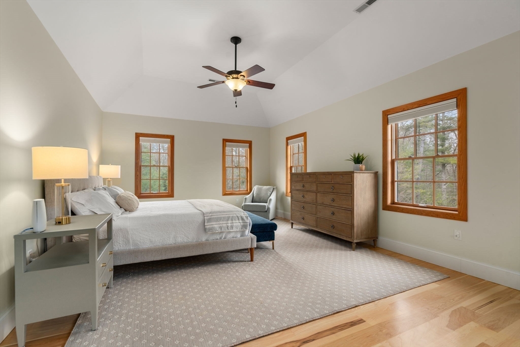 Staged bedroom with a large bed, wood dresser, and multiple wood-trimmed windows.