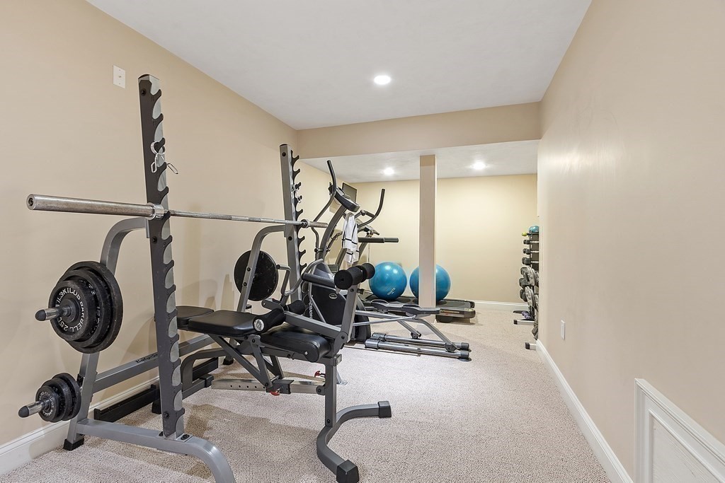 Basement home gym with a barbell rack, weight plates, an elliptical, and blue exercise balls.