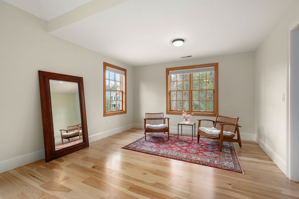 Sitting room with hardwood floors, wood-trimmed windows, a patterned rug, and two cushioned chairs.