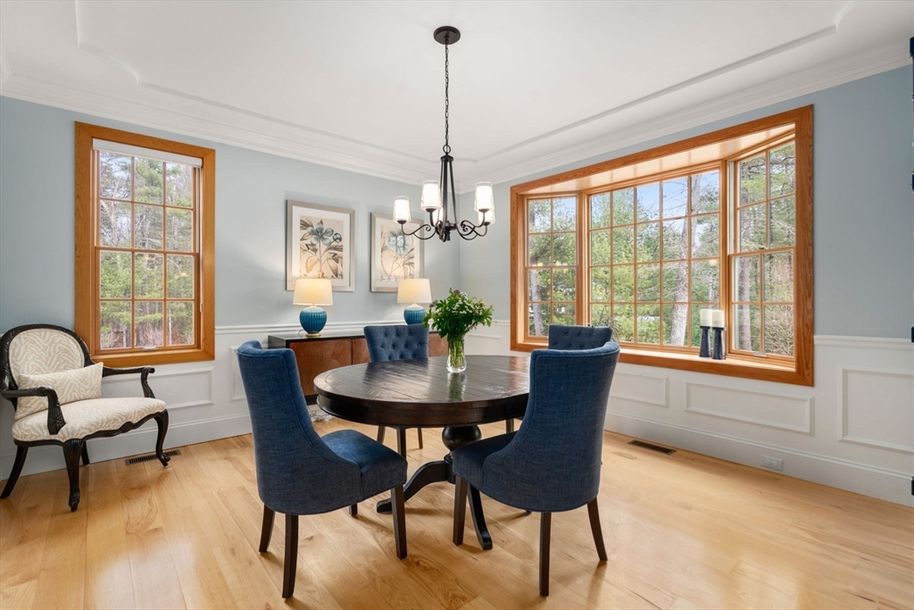 Dining room with a round wood table, blue chairs, and large windows overlooking trees.