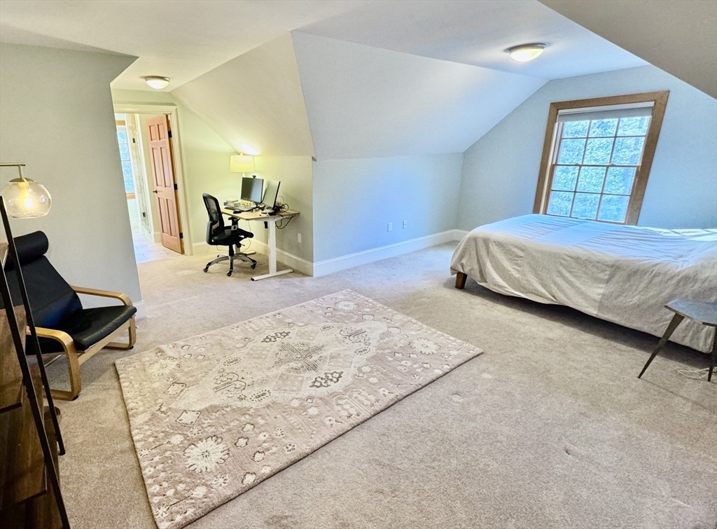 Attic bedroom with a bed beneath a large window, sloped ceiling, and desk area.