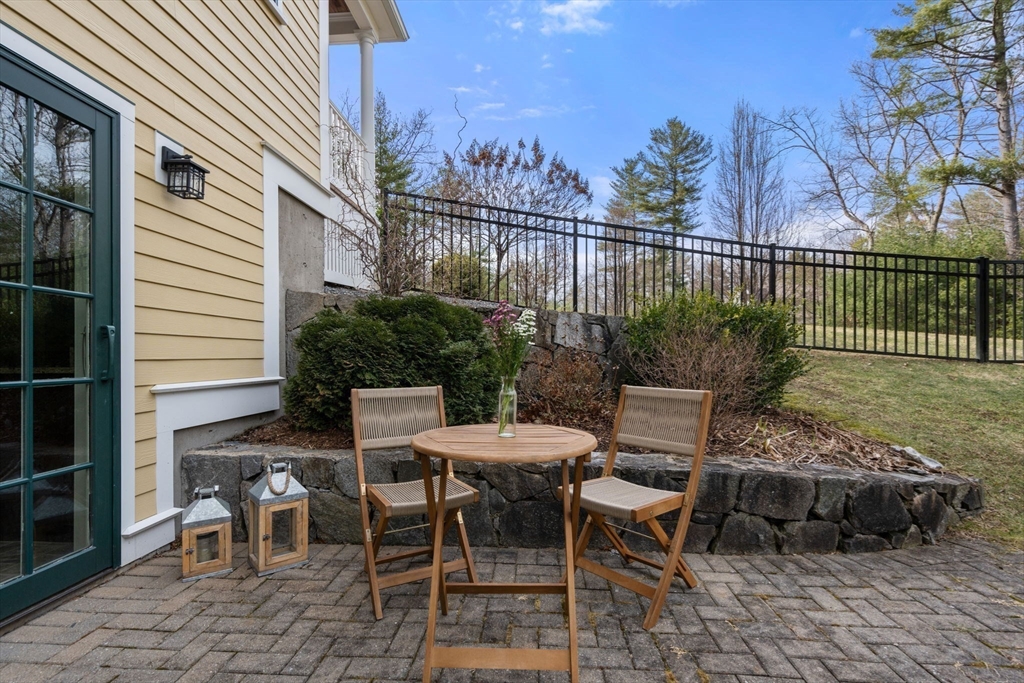 Stone patio with a wooden table and chairs beside a yellow-sided home and stone retaining wall.
