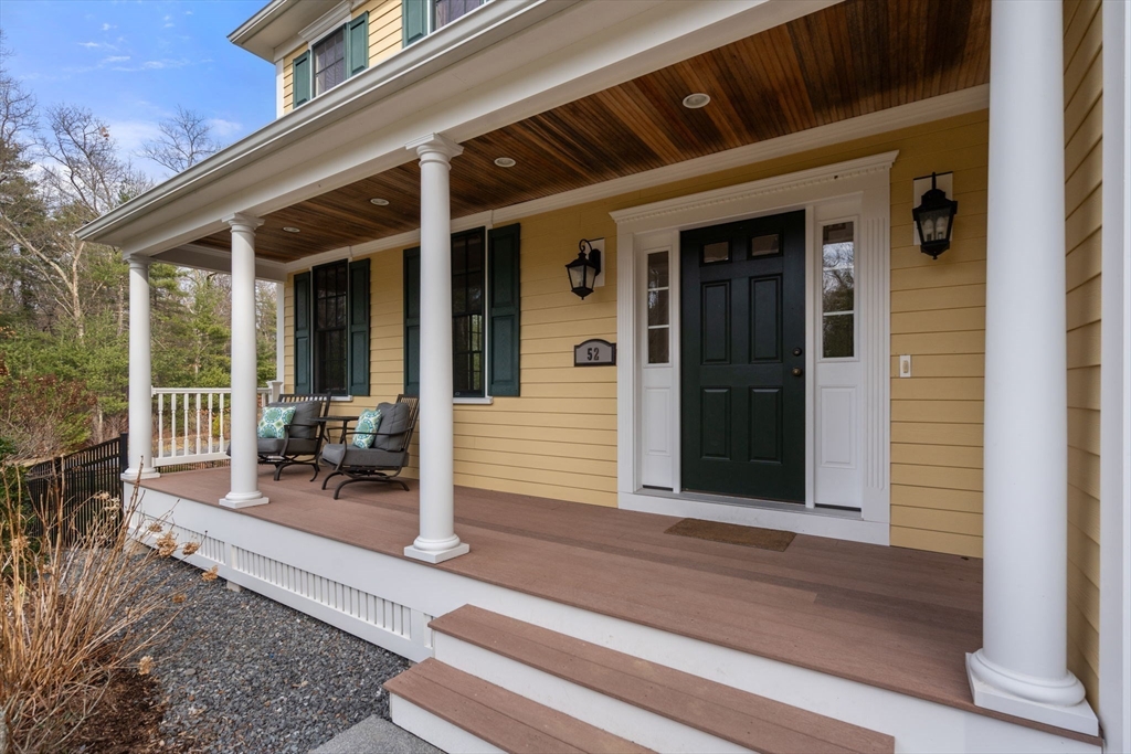 Yellow house entrance with a deep covered porch, white columns, and dark green door.