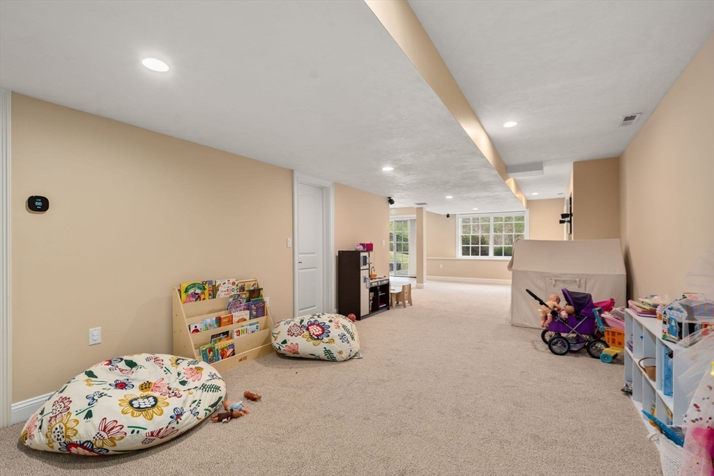 Spacious carpeted playroom with children’s books, toys, floor cushions, and windows at the far end.