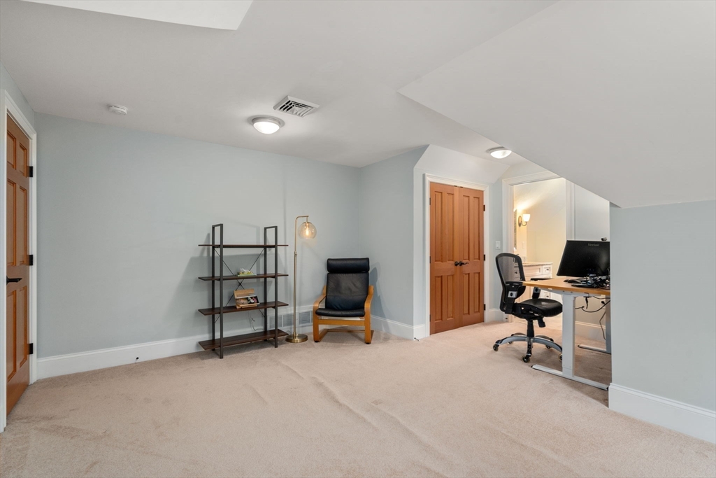 Finished attic office with a computer desk, black office chair, shelving, and wood-paneled door.