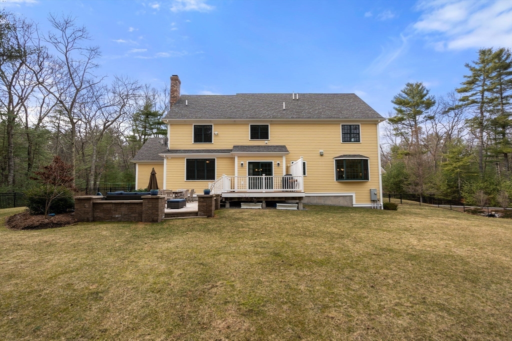 Rear of a yellow two-story house with a raised deck, stone patio wall, and broad lawn.
