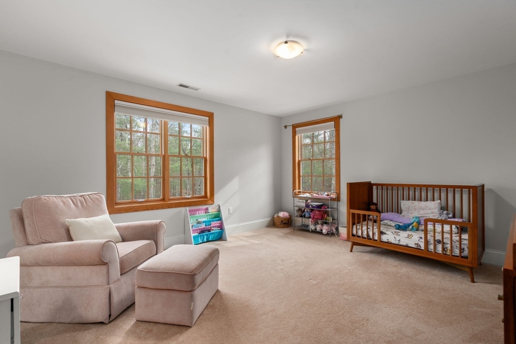 Nursery with a wooden crib, blush armchair, and wood-trimmed windows overlooking trees.