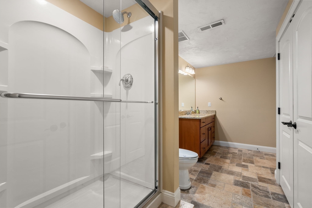 Bathroom with a glass-enclosed shower, wood vanity, and stone-look tile floor.
