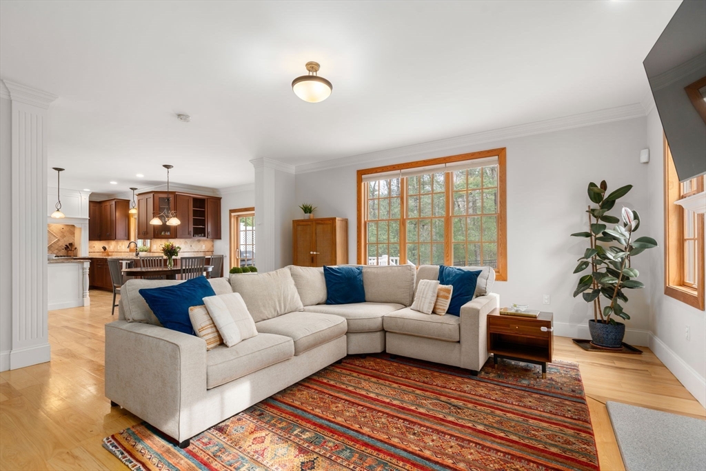 Living room with a cream sectional, colorful rug, and large wood-trimmed window overlooking trees.