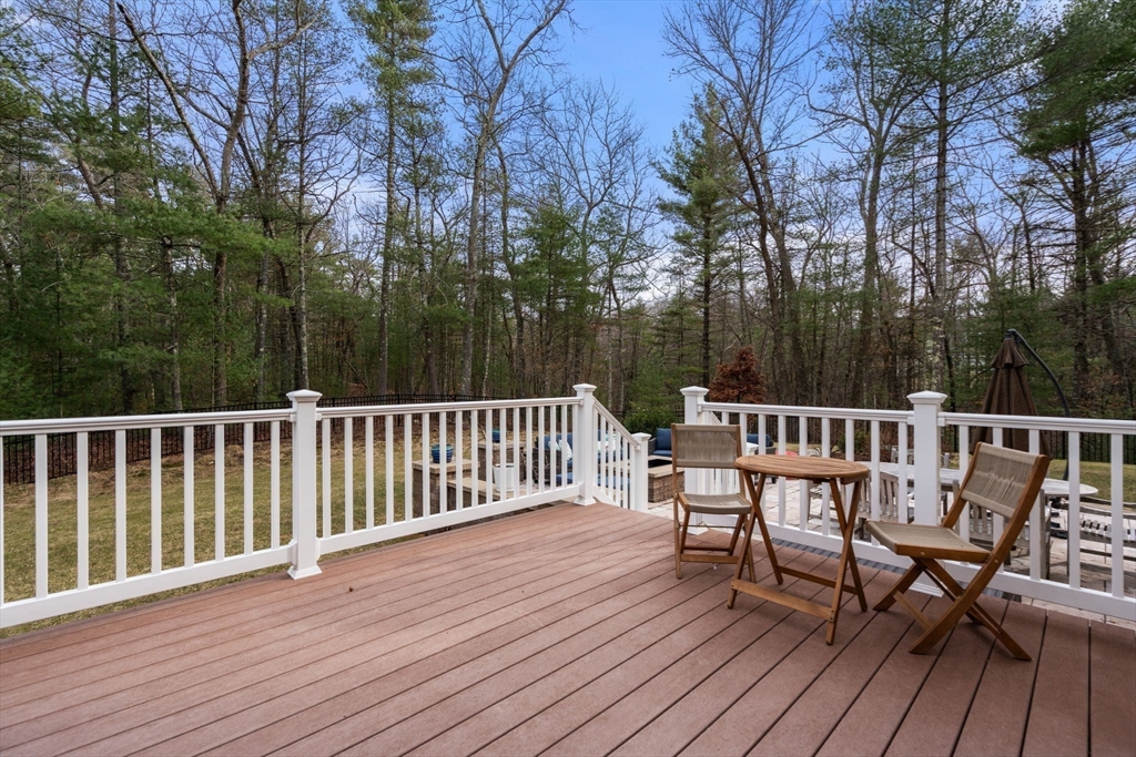 Deck with white railings and wooden patio furniture overlooking a wooded backyard.