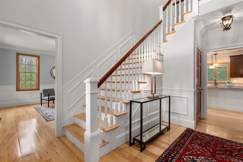 Entryway with a white paneled staircase, wood treads, glass console table, and patterned rug.