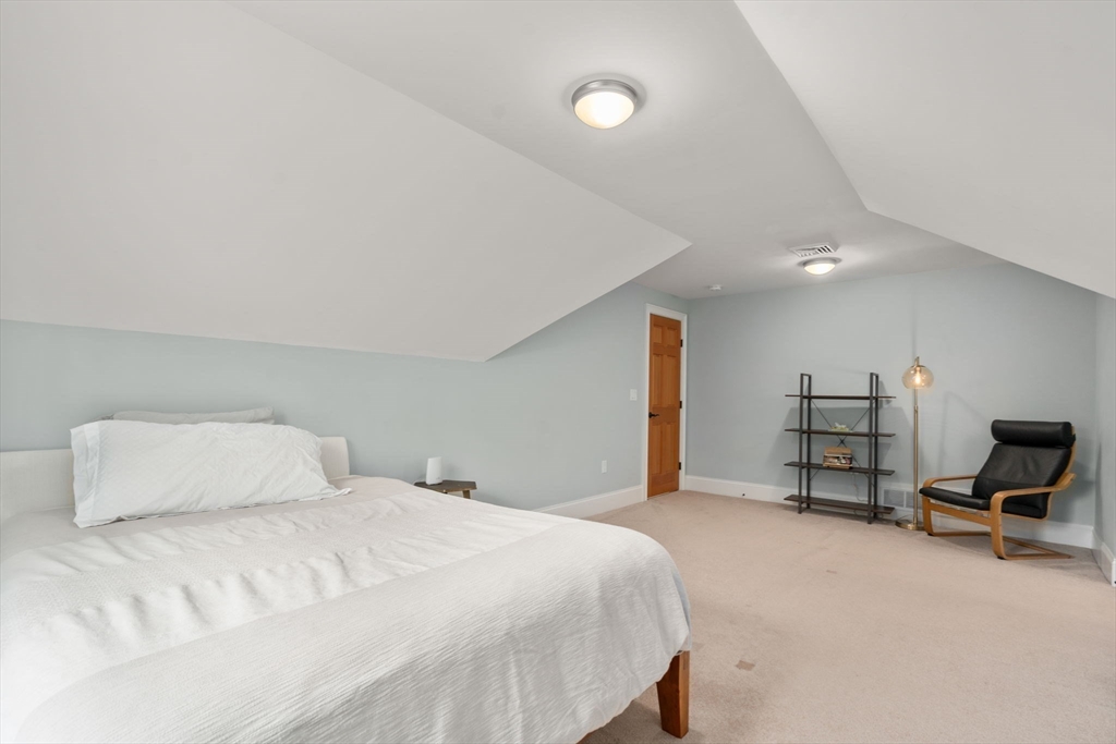 Furnished bedroom with a large white bed beneath a high sloped ceiling and a black lounge chair.