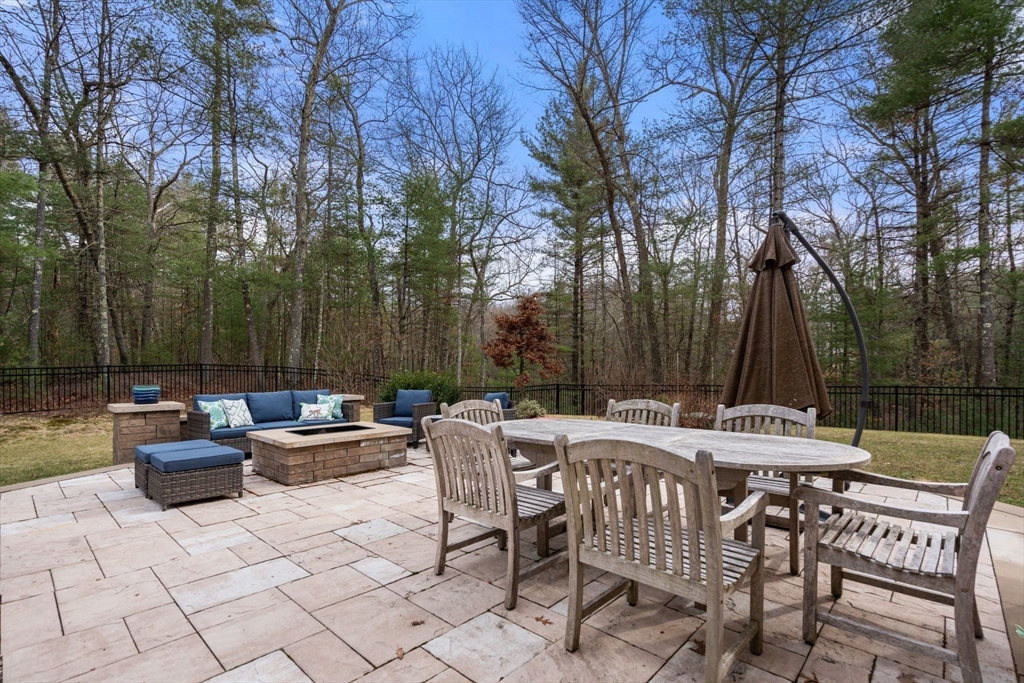 Stone patio with outdoor dining set and lounge seating beside a wooded backyard.