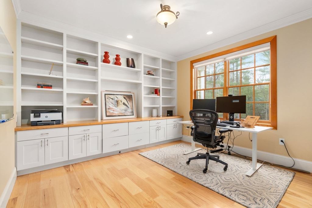 Home office with white built-in shelving, a computer desk, and a large window overlooking trees.