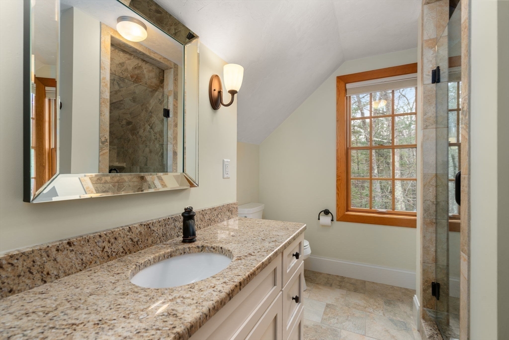 Bathroom with a granite vanity, tiled shower, and wood-trimmed window overlooking trees.