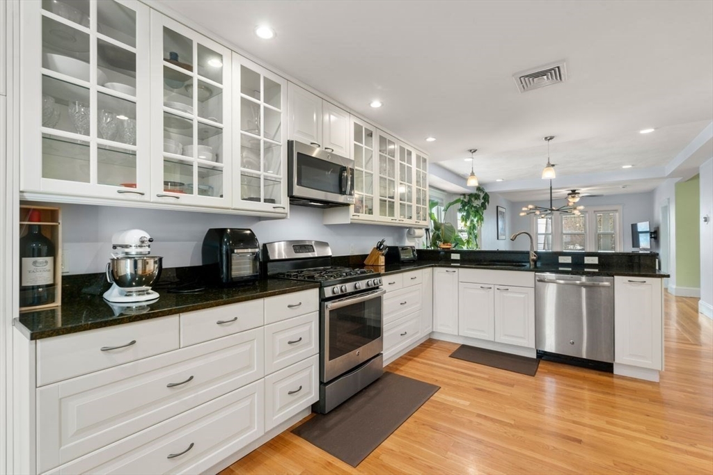 Kitchen with white glass-front cabinets, black countertops, stainless steel appliances, and hardwood floors.