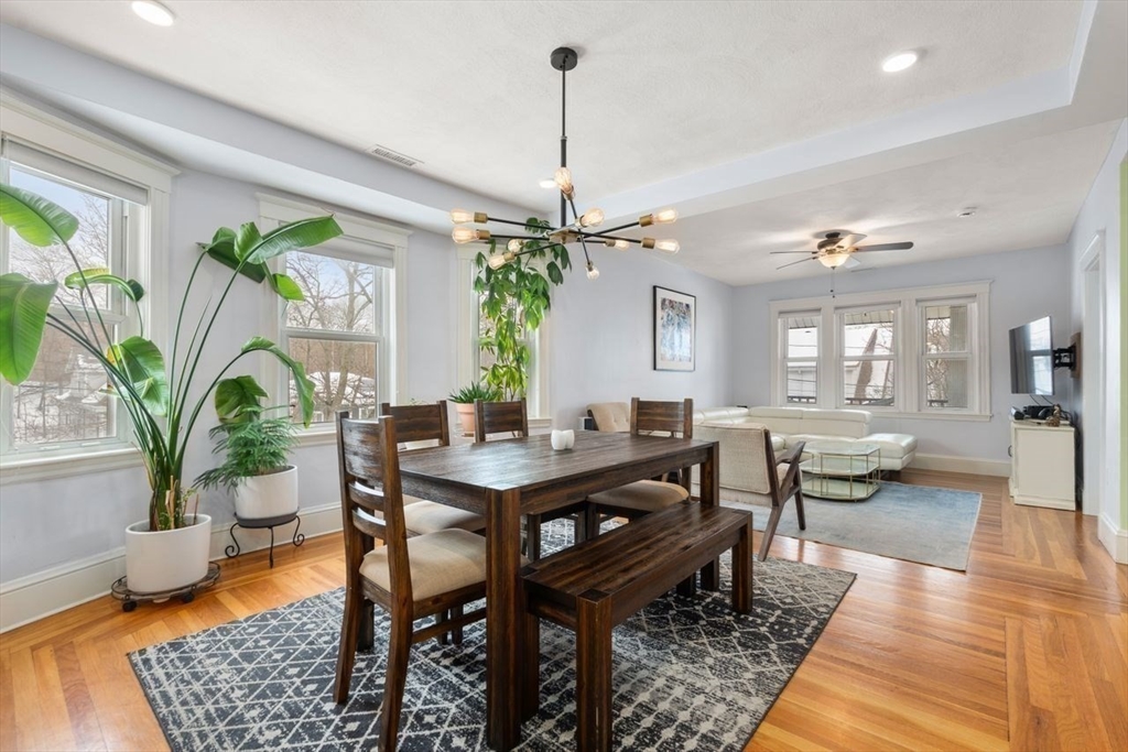Dining area with a dark wood table and bench, hardwood floors, large windows, and an adjoining living room.