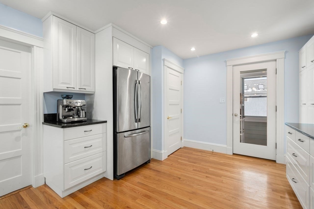 Kitchen with white cabinets, stainless steel refrigerator, black countertops, and hardwood floors.