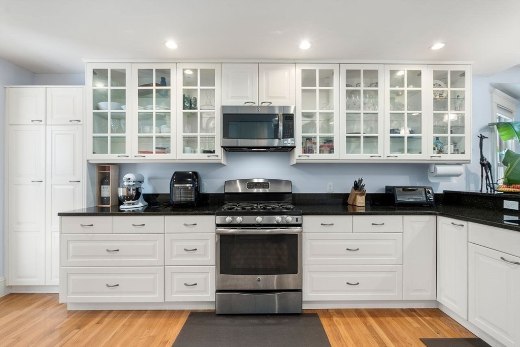 Kitchen with white glass-front cabinets, black countertops, stainless steel appliances, and hardwood floors.